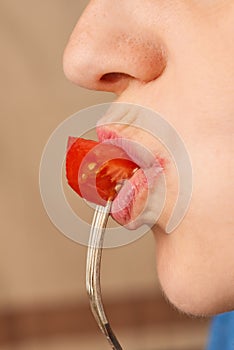 Close up happy Caucasian woman holding a fork and biting a slice of raw tomato. Side view. Low angle view