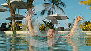 CLOSE UP: Happy Caucasian woman jumping out of pool glistens in exotic sun rays