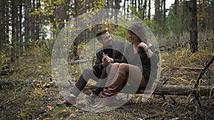 Close up of happy couple having a date in the forest. Smiling man and woman are sitting on the log among the trees