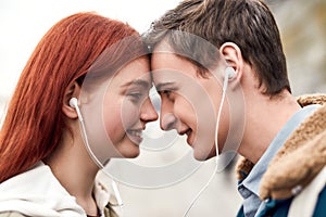 Close up of happy couple of teenagers listening to music using the same pair of earphones, looking at each other with