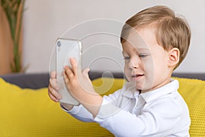 close-up happy little cute preschool baby boy talking video conference by smartphone in living room at home on yellow