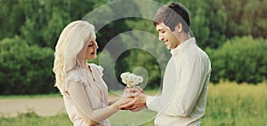 Close up of happy lovely young couple holding bouquet of wildflowers together over green summer background