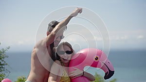 Close up of happy lover couple saddle swim inflatable pink flamingo