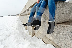 Close-up of a happy and loving couple foot traveler sitting on the granite waterfront. A pair in winter shoes and warm sweaters an