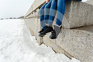 Close-up of a happy and loving couple foot traveler sitting on the granite waterfront. A pair in winter shoes and warm sweaters an