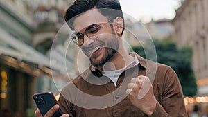 Close up happy lucky gen z Indian Arabian ethnic man guy male businessman student winner holding mobile phone pointing