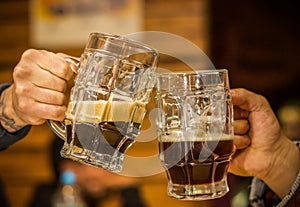 Close up of a happy male friends clinking with beer mugs in pub