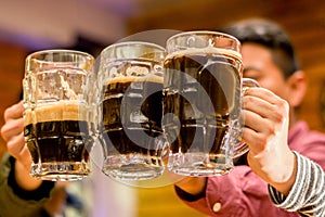 Close up of a happy male friends clinking with beer mugs in pub