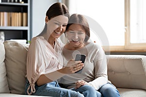 Close up happy mature mother and grownup daughter using phone