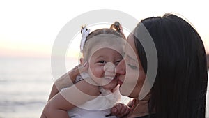 Close-up happy mother kissing baby daughter in sunrays as girl smiling hugging woman. Loving Caucasian parent and child