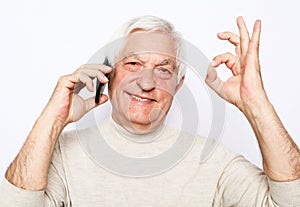 Close up of happy old man using smartphone and show ok desture over white background.