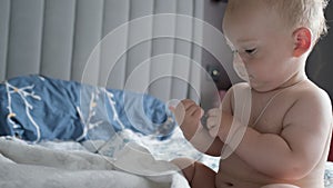 Close-up Happy playful kid 10 month old. Newborn boy bites the TV remote control on soft bed. baby child waking time