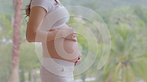 Close up Happy Pregnant Woman standing in front of nature mountain view and stroking her big belly with love,Pregnancy young woman