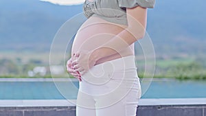 Close up Happy Pregnant Woman standing in front of nature mountain view and stroking her big belly with love,Pregnancy young woman