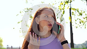 Close-up of happy red-haired girl talking on mobile phone outside on bright sunny day.
