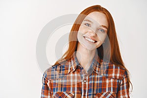 Close-up of happy redhead girl smiling at camera, standing on white background