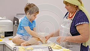 Close up of the happy smiled grandmother and grandson kneading a daugh together. slow motion of an elderly woman and