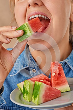 Close-up of a happy smiling Caucasian woman holding a slice of watermelon with her hand and biting it. Front view. Low angle view