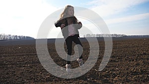 Close up of happy smiling girl with long blonde hair dances funny on plowed field at sunny day. Cheerful female child in