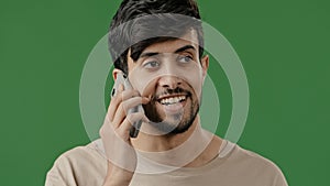 Close up happy smiling young arab guy in studio on green background talking using smartphone surprised positive man