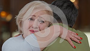 Close-up of happy surprised senior woman looking at camera with excited facial expression hugging man indoors. Portrait