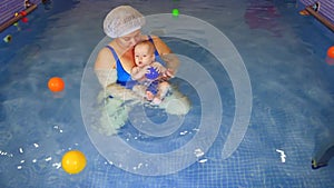 Close-up of a happy toddler learning to swim and swimming with an instructor in a children's pool. Infant swimming