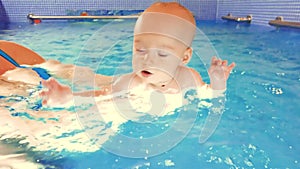 Close-up of a happy toddler learning to swim and swimming with an instructor in a children's pool. Infant swimming