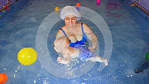 Close-up of a happy toddler learning to swim and swimming with an instructor in a children's pool. Infant swimming