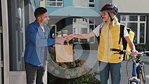 Close up of happy woman on a bike delivering coffee and food in paper bag to customer man home. Food delivery concept.