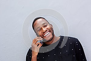 Close up happy young african man against wall talking on cell phone