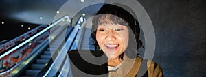 Close up of happy young asian girl, looks at her smartphone with surprised, excited face expression, reading good news