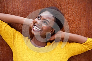 Close up happy young black woman smiling with hands behind head against brown background