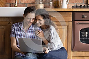 Close up happy young couple using laptop, sitting in kitchen