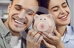 Close up of happy young family holding piggy bank indoors to save money for future.