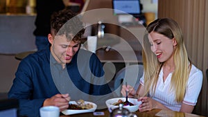 Close up of happy young girlfriend smiling and feeding her boyfriend indoors. Slow motion. Caucasian cheerful couple