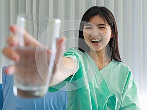 Close up of happy young inpatient woman  who is getting well from her ailment smiling on to camera and holding a glass of water in