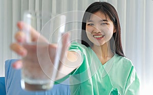 Close up of happy young inpatient woman  who is getting well from her ailment smiling on to camera and holding a glass of water in