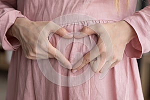 Close up happy young pregnant woman making love sign.