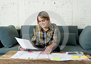 Close up of happy young woman sitting on the sofa surrounded by papers calculating and paying bills