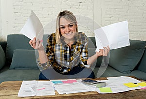 Close up of happy young woman sitting on the sofa surrounded by papers calculating and paying bills