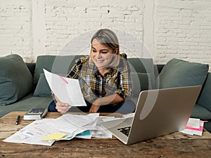 Close up of happy young woman sitting on the sofa surrounded by papers calculating and paying bills