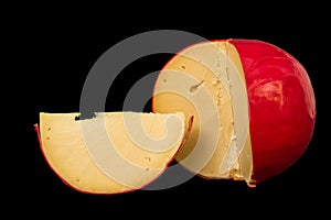 Close up. Head of cheese Edam in a red wax shell. Nearby is a cut piece. Isolated on black background