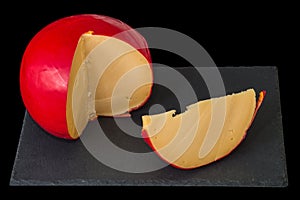 Close up. Head of Dutch cheese Edam and sliced piece on black chopping board. Isolated on black background