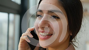 Close up head shot Arabian girl talking mobile phone near window smiling female businesswoman lady speak business call