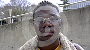 Close up head shot of confident young black man looking at camera with serious expression in the street. 4k video