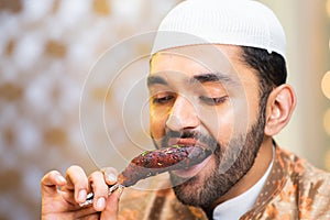 Close up head shot of muslim man eating chicken leg piece during ramadan festival feast