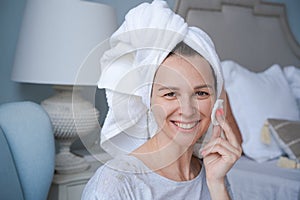 Close-up head shot smiling beautiful woman wrapped in towel applying toner