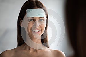 Smiling young brunette woman applying moisturizing patch on forehead. photo