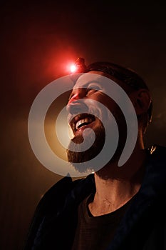 Close-up head-shot of young bearded extreme man with red head lamp on forehead