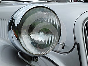 Close up of the headlamp of an elegant silver colored stylish 1930s vintage automobile